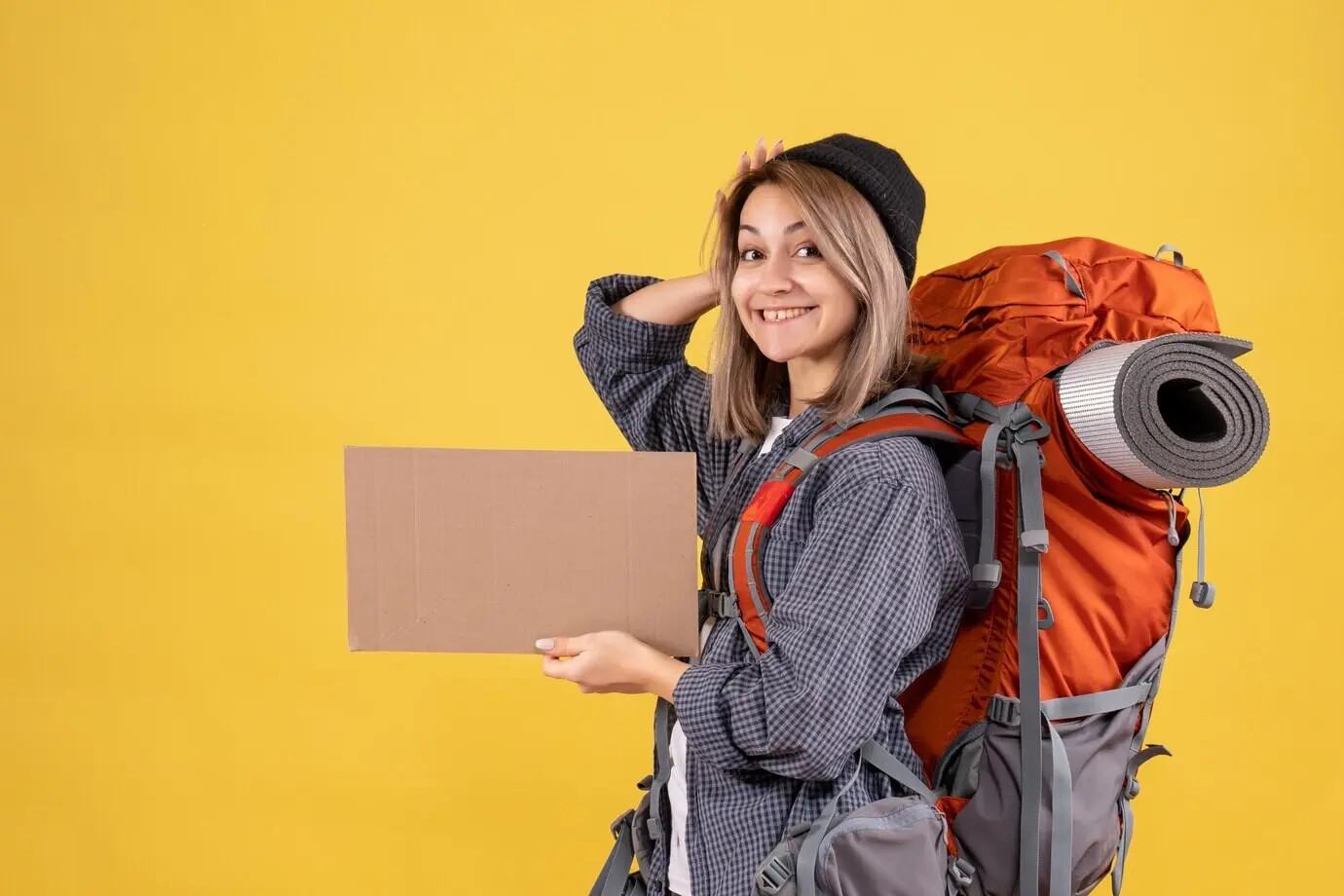 Vorderansicht einer fröhlichen Reisenden mit rotem Rucksack, die Pappe in der Hand hält.