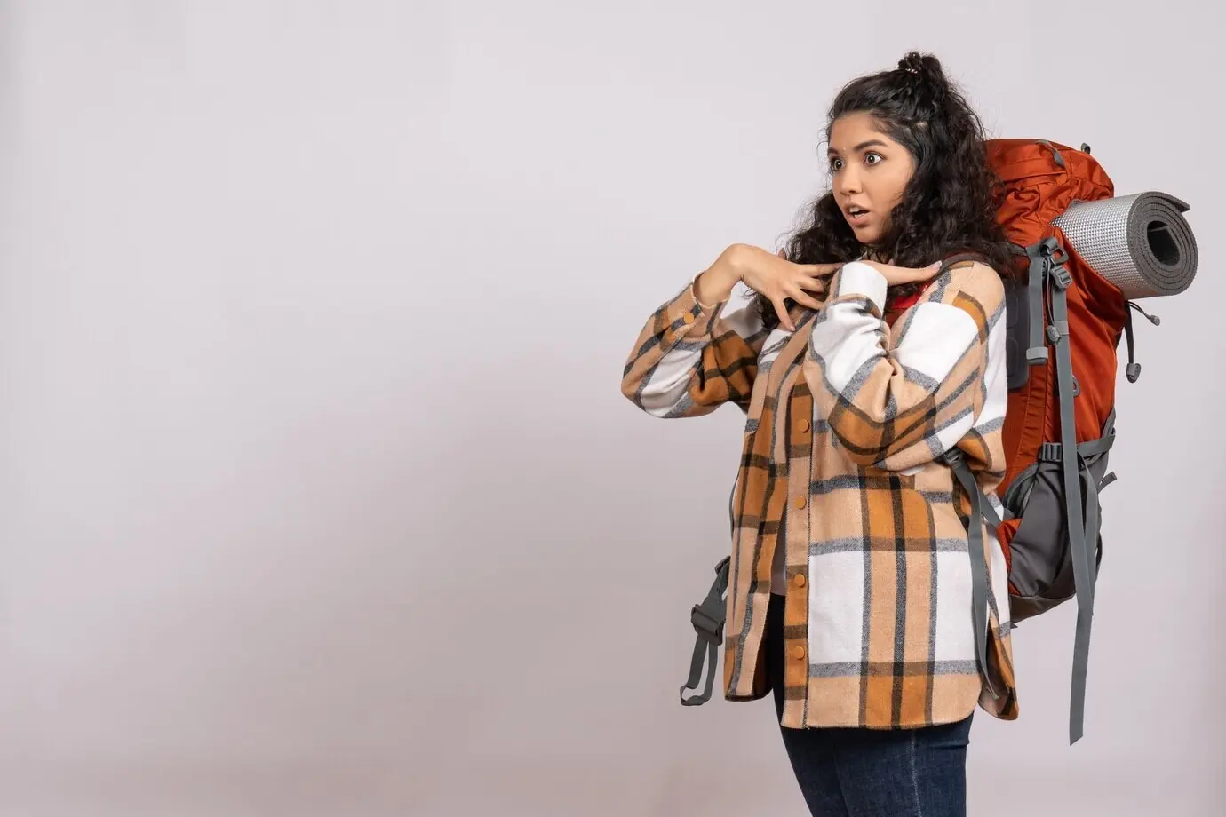 Vorderansicht einer jungen Frau, die mit Rucksack wandern geht, vor weißem Hintergrund; Waldausflug, Bergluft, Touristin, Campus, Urlaub.