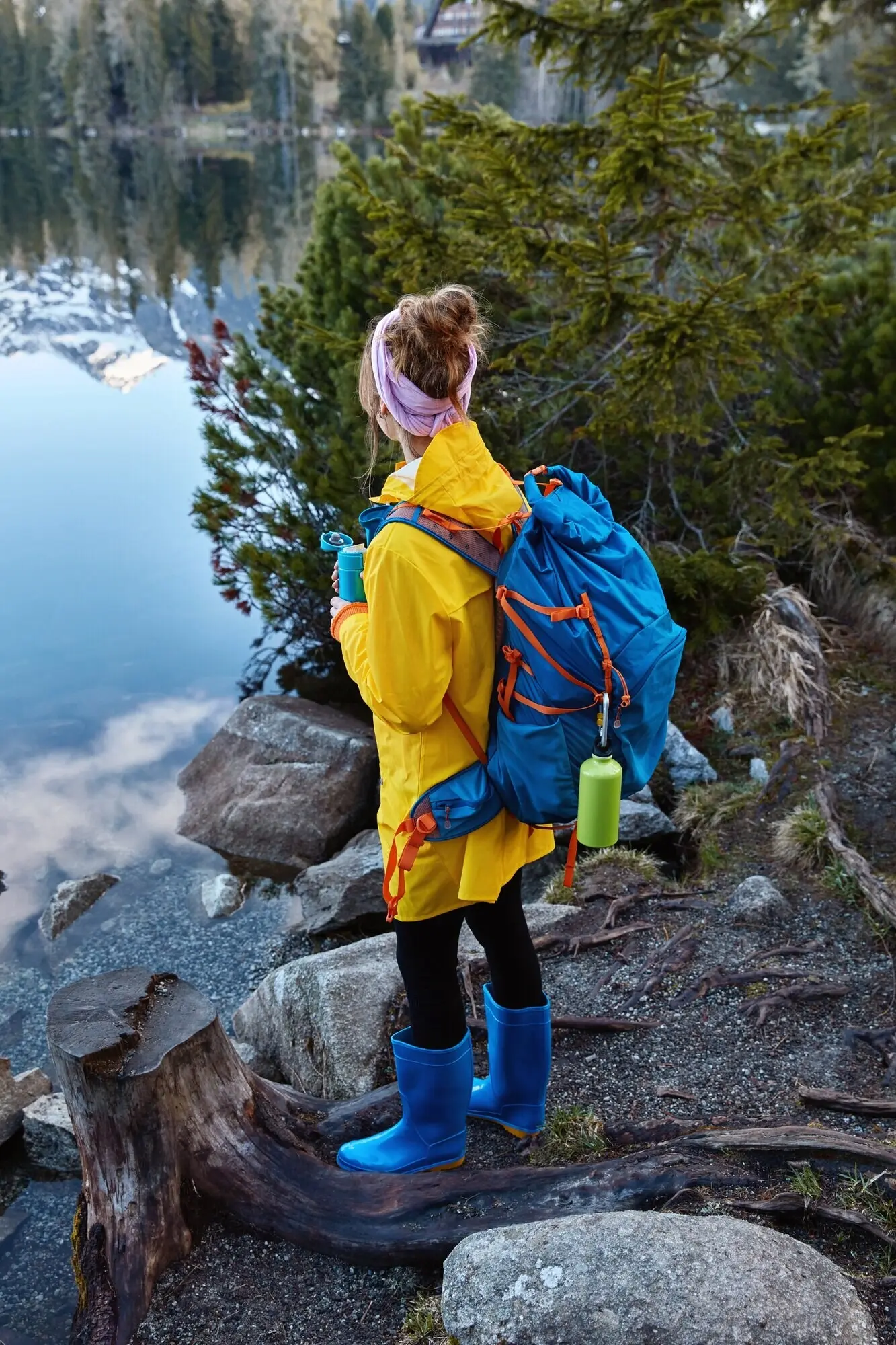 Außenaufnahme einer weiblichen Reisenden, die den Panoramablick auf einen Bergsee genießt, sich nach einem Spaziergang ausruht und dabei heißen Tee trinkt, einen großen Rucksack trägt und auf Urlaubsreise ist.